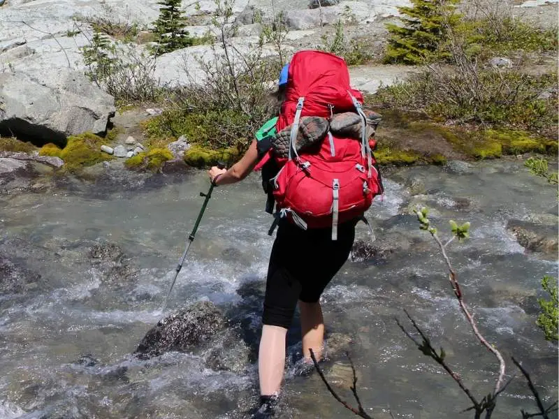 Pros and Cons of Trekking Poles: What You Need to Know woman hiking across a stream with poles
