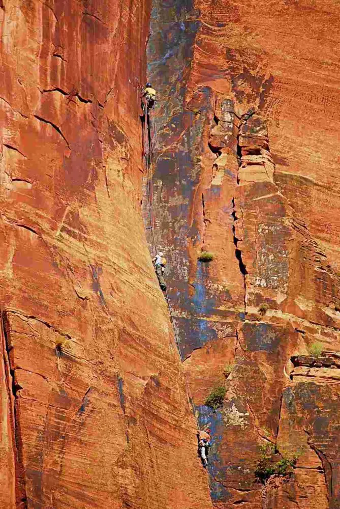 Three men climbing in tall rock cliffs in Zion National Park